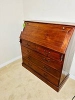 Full view of the closed antique wood secretary desk showing four large drawers and the drop-front panel with brass knobs and pulls.