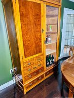 Front left perspective showing the solid wood door on the left side, glass display door on the right, and multiple drawers at the bottom with brass hardware.