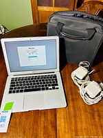 MacBook Air on wooden table next to two Apple power adapters and black carrying bag