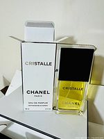 Chanel Cristalle Eau de Parfum bottle with black cap and yellow liquid alongside its original white box with black text.