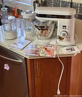 Stand mixer, food processor bowl, blender jar, manuals displayed on countertop