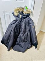 Full view of black Fjällräven women's winter jacket with faux fur-trimmed hood hung on door