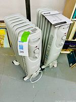 Two white Garrison oil-filled heaters standing side by side on the floor with instruction manual on top of one heater.