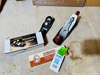 Two metal hand planes, one with red knob and handle, one with silver knob, alongside boxed sharpening systems on a workbench.