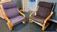 Pair of two IKEA POÄNG armchairs with bentwood birch veneer frames and dark fabric cushions, situated on carpeted floor.