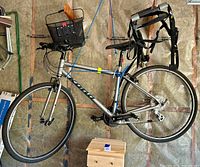 Full side view of the silver Kona hybrid road bike hanging, showing flat handlebars with basket, aluminum frame, drivetrain and rear rack