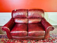 Front view of the burgundy leather loveseat on a patterned rug against a red wall