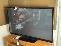 Front view of the LG plasma TV placed on a wooden surface with remote control beside it, showing the screen and stand.