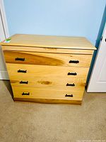 Front view of the solid wood dresser showing four drawers with distinct wood grain and black metal pulls.