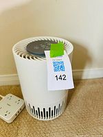 Front view of TaoTronics cylindrical white air purifier with control panel on top and auction tag attached.