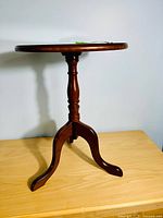Side view of the cherry pedestal accent table showing round top and tripod base with turned central column