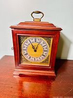 Front view of vintage Howard Miller cherry mantle clock showing wood case, brass handle on top, and clock face with Roman numerals.