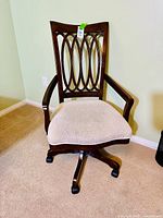 Front view showing decorative wooden backrest, armrests, beige upholstered cushioned seat, casters at base.