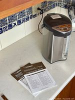 Zojirushi water boiler and warmer on countertop, with manuals beside it