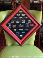 Framed display of 20 WrestleMania enamel pins arranged with labels on black matte inside a diamond shaped frame.