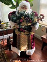 Full view of Santa Claus figure standing with greenery arrangement and candy cane inside the arms.