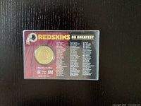 Front and back of the 80th Anniversary Washington Redskins token in plastic casing showing team logo, token, and list of 80 greatest players.