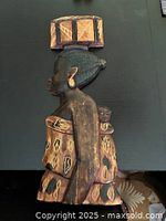 Side view of the wooden carving showing the woman carrying a baby with detailed patterns on the cloth and earrings.