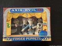 Front view of unopened Axis of Evil III finger puppets box showing four caricature finger puppets behind plastic window.
