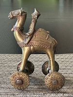 Side view of brass figurine showing man sitting on a camel with wheels, highlighting details on the camel's saddle and wheels.