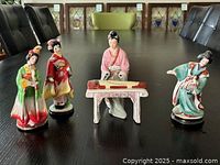 Four ceramic Asian figurines arranged on a table, showing front and side views