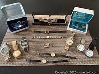 Collection of watches displayed on a table, including digital and analog wristwatches and pocket watches, some in branded boxes.