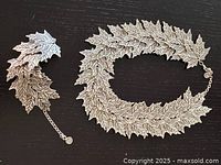 Costume necklace laid out in a circle showing leaf shaped links and detailed engraved vein patterns on black surface.