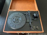 Record player in wooden case with visible turntable platter, tonearm, and control knobs. Power adapter included.