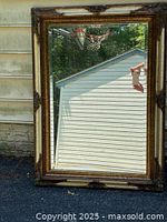 Full view of the framed mirror showing the dark, ornate wooden frame with carved corner accents reflecting back a garage and outdoor basketball hoop.