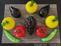 Top view of 10 glass fruit pieces including pears, apples, grapes, tomatoes, and peas arranged on woven placemat.