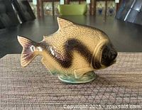 Front view of a ceramic decorative fish with brown and tan glazing, placed on a woven table mat.