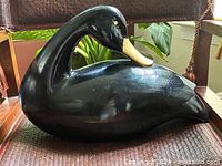 Front angle view of the black wooden swan placed on a woven surface, showcasing the swan's curved neck and gold beak.