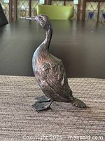 Front view of metal goose figurine standing upright with detailed feather texture and realistic feet.
