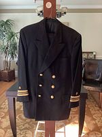 Front view of Navy officer's black double-breasted jacket with gold buttons and sleeve insignia on cuffs.