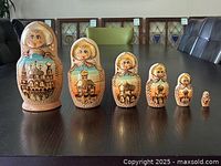 Six wooden Russian nesting dolls arranged in descending size order on a table, showing faces and architectural paintings.