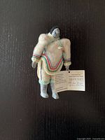 Full view of the signed Indigenous stone face doll with traditional clothing and original tag attached.