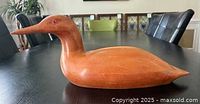 Wooden duck sculpture placed on a table showing side profile, smooth natural wood finish, and red eyes.