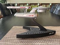 Side view of the Star Trek USS Enterprise telephone model mounted on a black base stand with 'STAR TREK' label