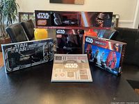 Photo of entire Star Wars memorabilia collection showing unopened boxes of the light up Darth Vader helmet, 2018 collector's edition calendar, Disney chess set, Escape From Death Star game, and light-up Darth Vader hand with lightsaber.