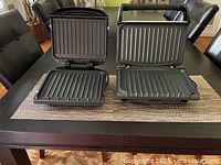 Two George Foreman electric grills with lids open, showing ridged cooking plates inside.
