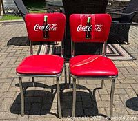 Pair of red Coca Cola branded chairs with chrome frames photographed outside on a patio.