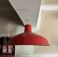 Red vintage metal hanging light fixture hanging from a ceiling hook, showing the wide flared metal shade and hanging mechanism.