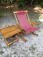 Wooden rocking chair and folding table set outdoors on dirt and grass surface.