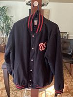 Front view of black Washington Nationals jacket with red and black striped ribbed collar, cuffs and hem, showing the small 'W' logo on chest.