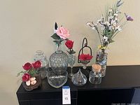 View of the full lot including several glass vases, heart-shaped glass bowl, and multiple faux flower arrangements with pebble decor inside some vases.