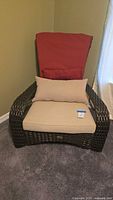 Front-facing photo of the dark brown synthetic wicker patio chair with cushions in beige and red.