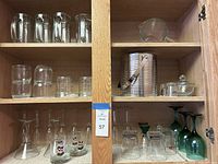 Wide view of wooden cabinet shelves displaying various glassware including pitchers, an ice bucket, and multiple styles of glasses.