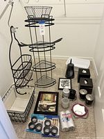 Full view of bathroom items set including black metal standing shower caddy with multiple shelves, wire baskets, tissue boxes, wall art, various holders, mirror, and other accessories all arranged on carpeted floor with white walls.