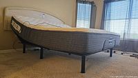 Side angle view of the king size adjustable bed frame with mattress, showing the height and structure of the bed and partially visible wired remote control on mattress.