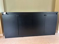 Front view of black cabinet showing three closed doors and simple round knobs.